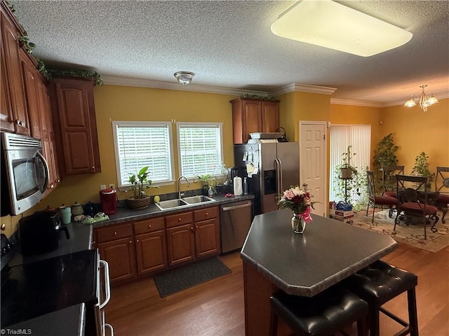kitchen with appliances with stainless steel finishes, a sink, dark countertops, wood finished floors, and a kitchen island