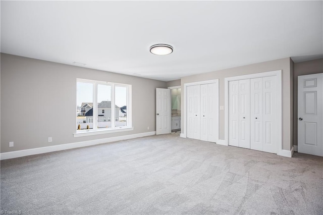 unfurnished bedroom featuring multiple closets and light carpet