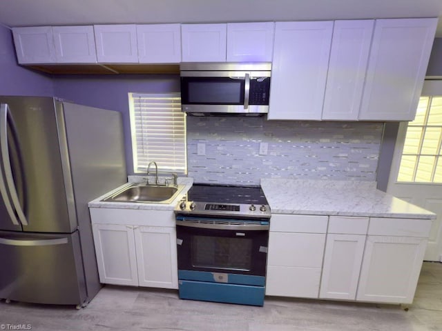 kitchen featuring sink, white cabinets, backsplash, stainless steel appliances, and light stone countertops