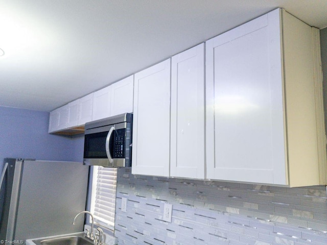 interior details with white cabinetry, refrigerator, sink, and tasteful backsplash