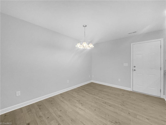 spare room featuring a chandelier, visible vents, light wood-type flooring, and baseboards