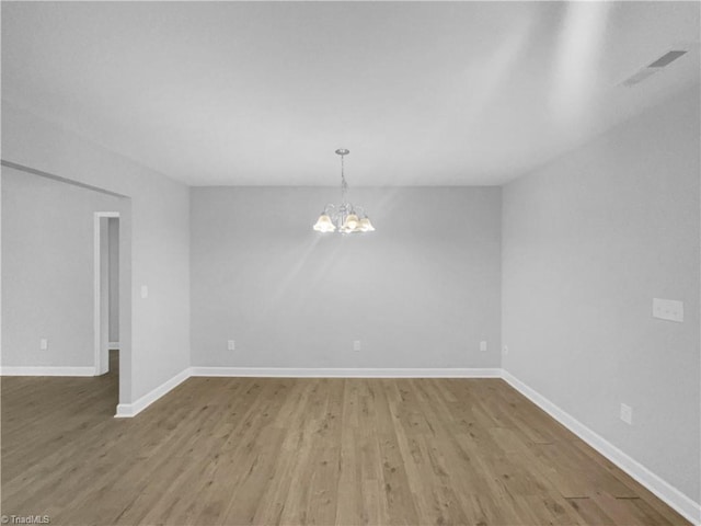 empty room featuring visible vents, baseboards, an inviting chandelier, and wood finished floors