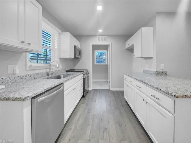 kitchen with visible vents, light wood-style flooring, a sink, stainless steel appliances, and white cabinets