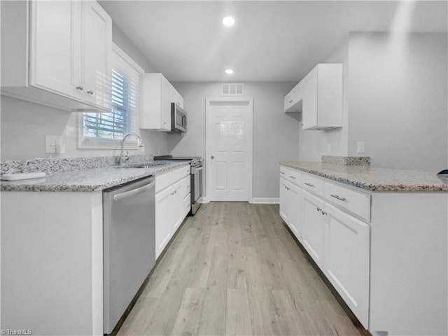 kitchen with light stone counters, a sink, white cabinets, appliances with stainless steel finishes, and light wood-type flooring