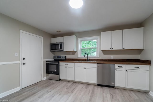 kitchen featuring white cabinets, wooden counters, stainless steel appliances, and sink