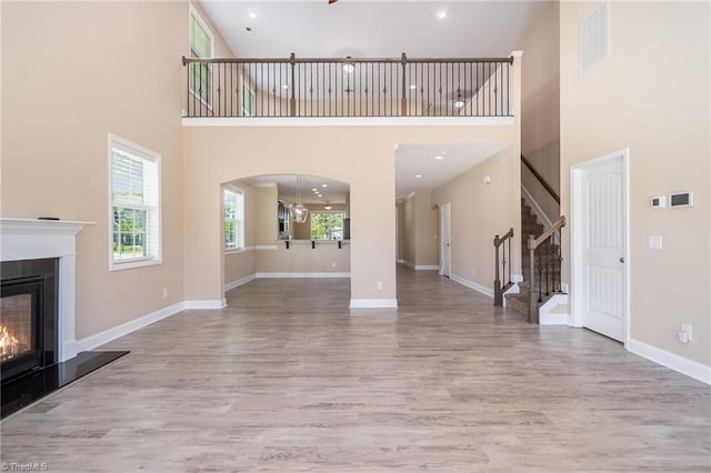 2209 Starfall Dr, Colfax, NC 27235 - unfurnished living room with wood finished floors, a glass covered fireplace, a high ceiling, stairs, and recessed lighting
