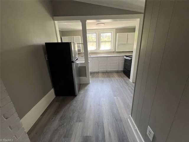 kitchen featuring wood-type flooring, white cabinets, stainless steel fridge, range with electric cooktop, and lofted ceiling