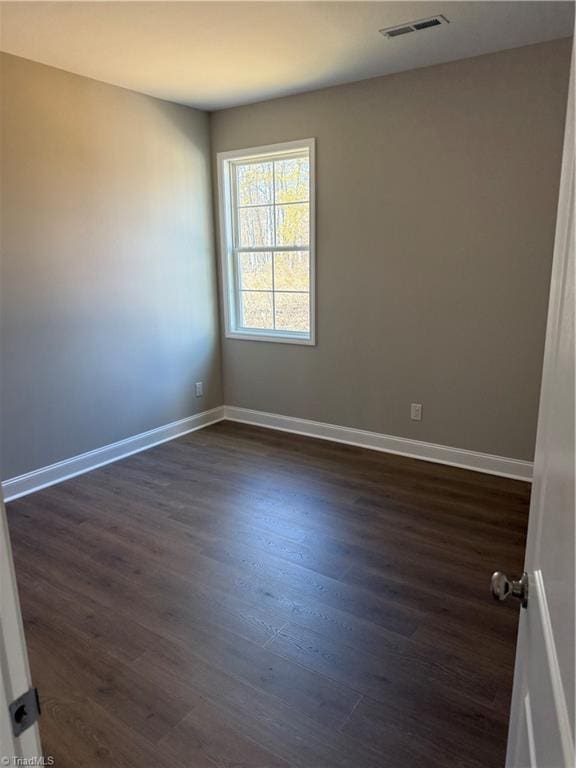 empty room featuring visible vents, baseboards, and dark wood-style floors