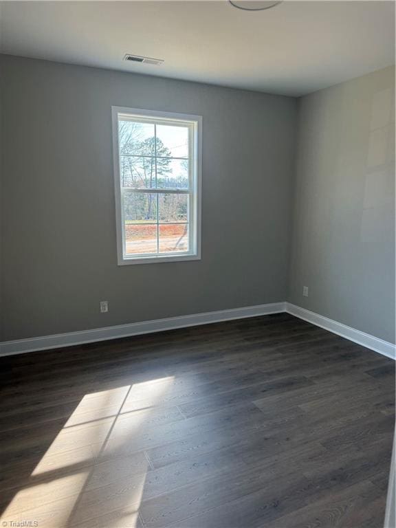 unfurnished room featuring dark wood-style floors, visible vents, and baseboards