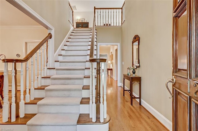 staircase featuring crown molding, a high ceiling, and hardwood / wood-style floors