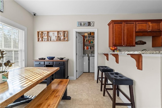 kitchen with light tile patterned flooring, a kitchen bar, separate washer and dryer, and light stone counters