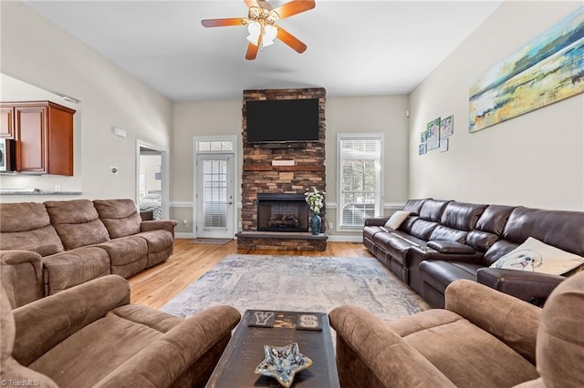 living room featuring ceiling fan, a stone fireplace, and light wood-type flooring