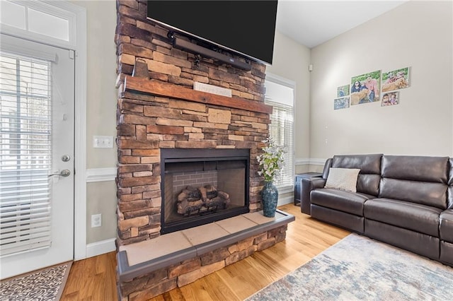 living room with a stone fireplace, wood-type flooring, and a healthy amount of sunlight