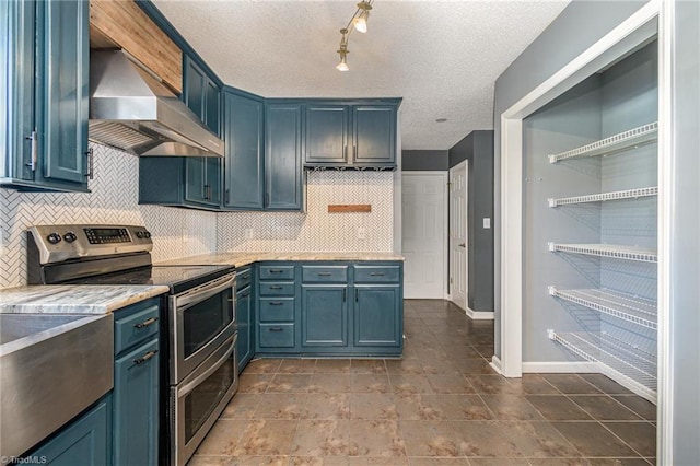 kitchen featuring wall chimney range hood, blue cabinetry, backsplash, a textured ceiling, and range with two ovens