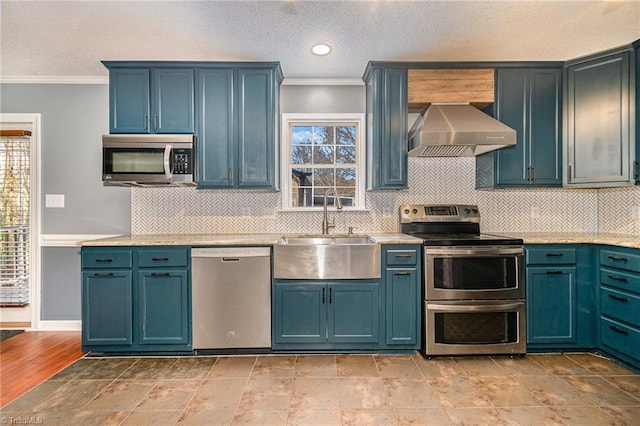 kitchen with appliances with stainless steel finishes, sink, wall chimney range hood, and blue cabinetry