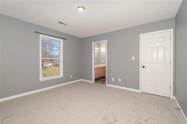 unfurnished bedroom with ensuite bath, carpet floors, and a textured ceiling