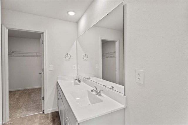 bathroom with a walk in closet, a sink, baseboards, and double vanity