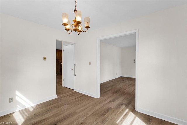 spare room with baseboards, an inviting chandelier, and wood finished floors