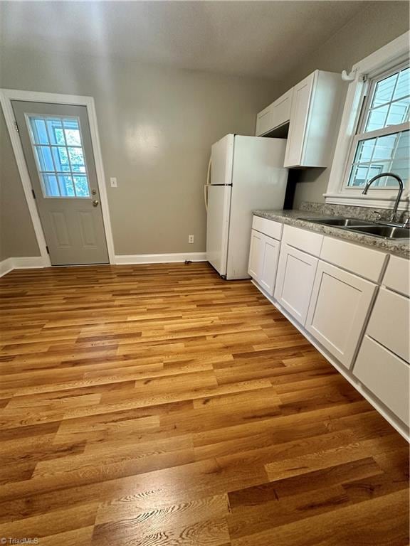 kitchen featuring light wood-type flooring, white cabinetry, sink, and white fridge