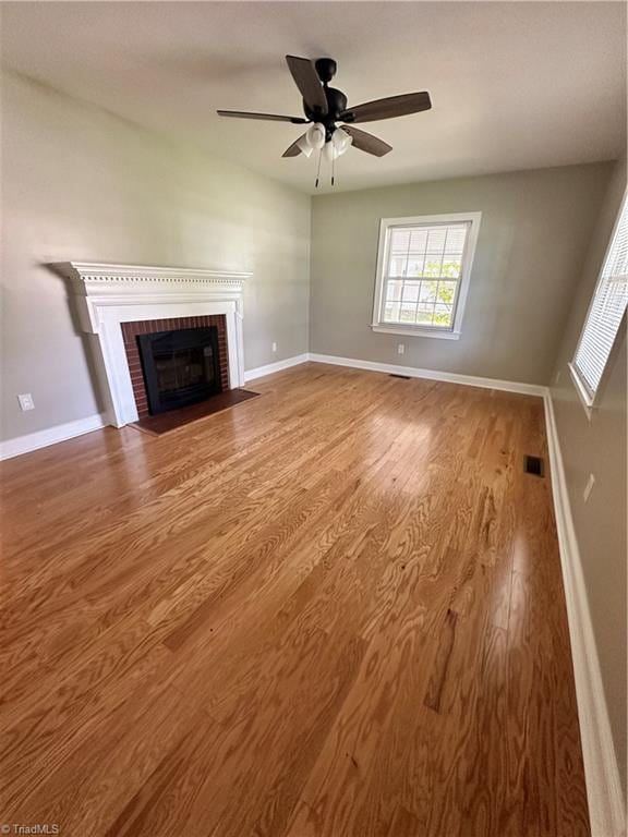 unfurnished living room with ceiling fan, a brick fireplace, and hardwood / wood-style flooring