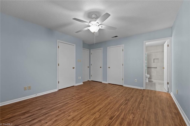 unfurnished bedroom featuring ensuite bath, ceiling fan, hardwood / wood-style floors, a textured ceiling, and two closets