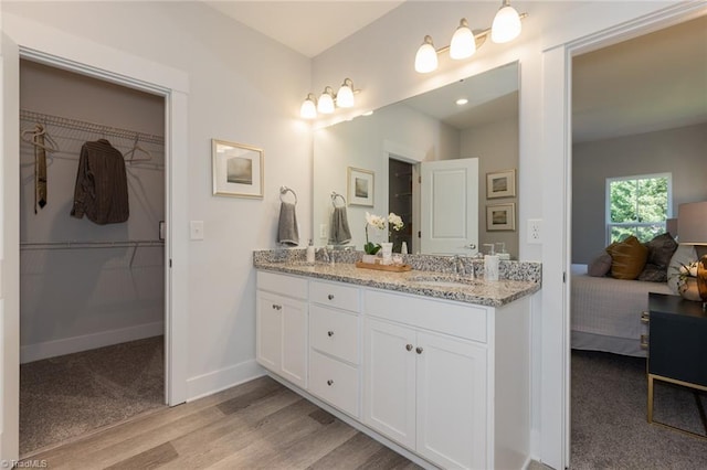 ensuite bathroom with wood finished floors, baseboards, double vanity, and a walk in closet