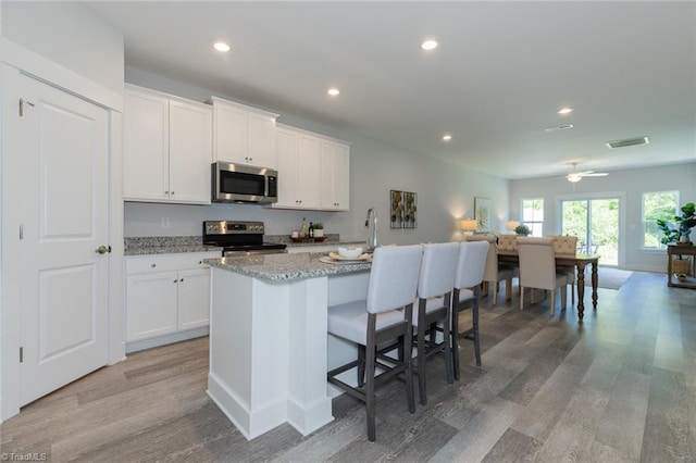 kitchen with stainless steel appliances, light wood-style flooring, a kitchen island with sink, recessed lighting, and white cabinetry