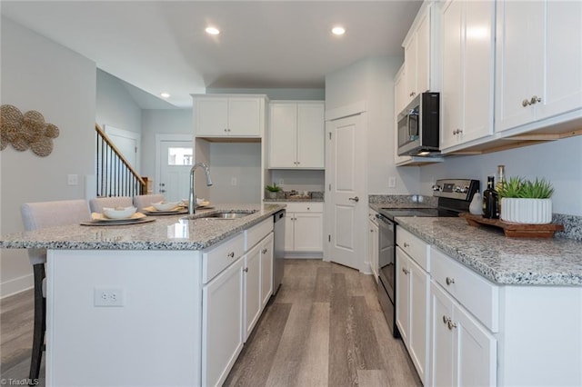 kitchen featuring appliances with stainless steel finishes, a sink, light wood-type flooring, white cabinetry, and recessed lighting