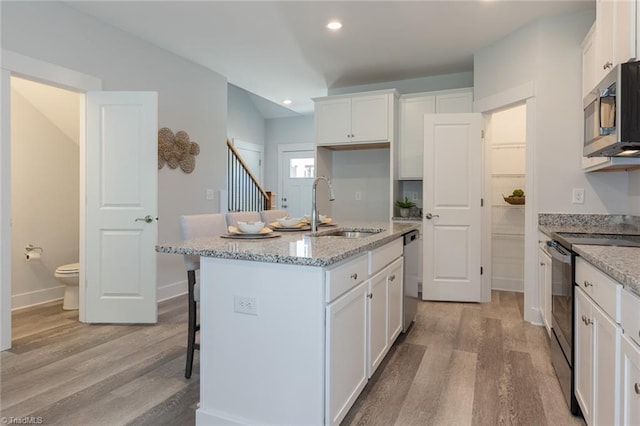 kitchen with a sink, appliances with stainless steel finishes, light wood finished floors, white cabinetry, and recessed lighting