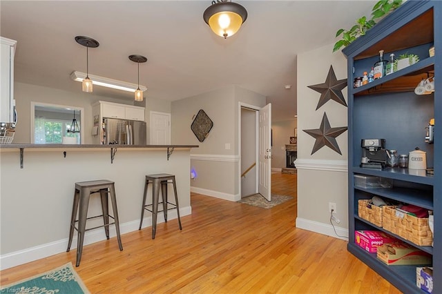 kitchen with decorative light fixtures, freestanding refrigerator, white cabinets, light wood-type flooring, and a kitchen bar