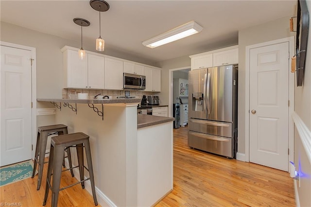 kitchen with stainless steel appliances, a breakfast bar, a peninsula, white cabinets, and dark countertops