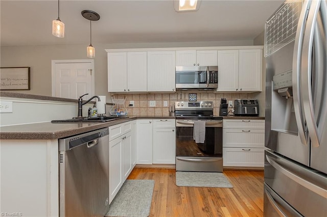 kitchen featuring a peninsula, a sink, appliances with stainless steel finishes, tasteful backsplash, and dark countertops