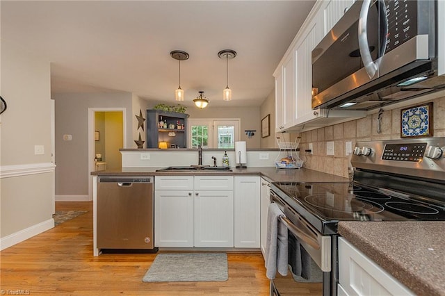 kitchen with light wood-style flooring, stainless steel appliances, a peninsula, a sink, and white cabinets