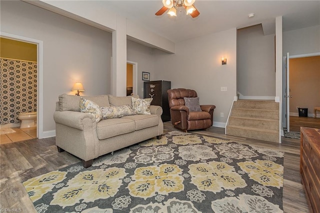 living room featuring ceiling fan, stairs, baseboards, and wood finished floors