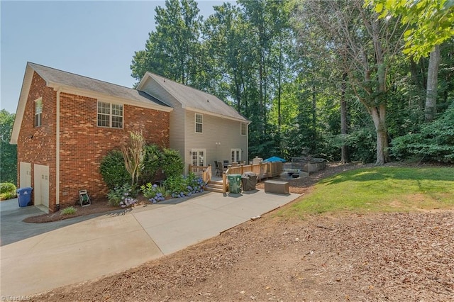 rear view of house with a deck, an attached garage, brick siding, concrete driveway, and a lawn