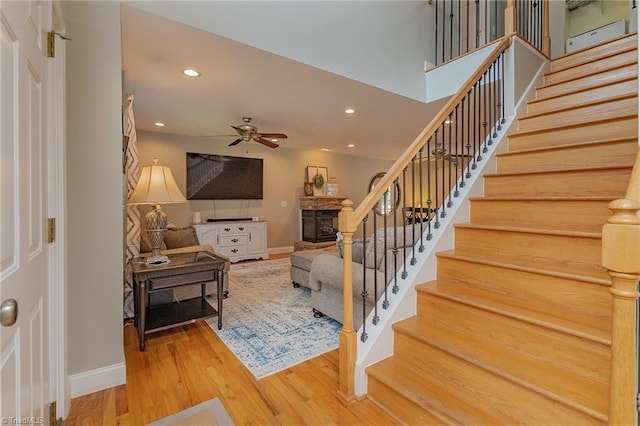 interior space featuring recessed lighting, a fireplace with raised hearth, a ceiling fan, wood finished floors, and baseboards