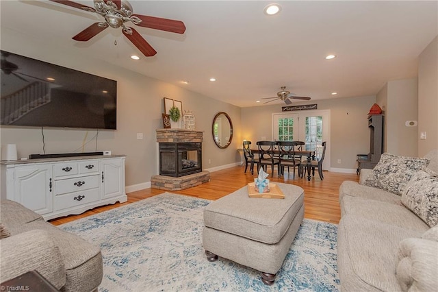 living room with baseboards, a ceiling fan, a stone fireplace, light wood-style floors, and recessed lighting