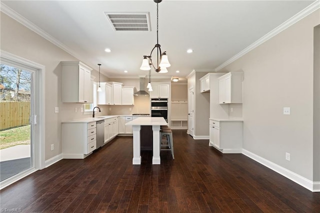 kitchen with white cabinetry, a kitchen island, appliances with stainless steel finishes, wall chimney range hood, and pendant lighting