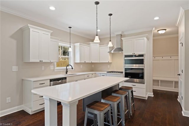 kitchen with appliances with stainless steel finishes, a center island, pendant lighting, wall chimney range hood, and white cabinets