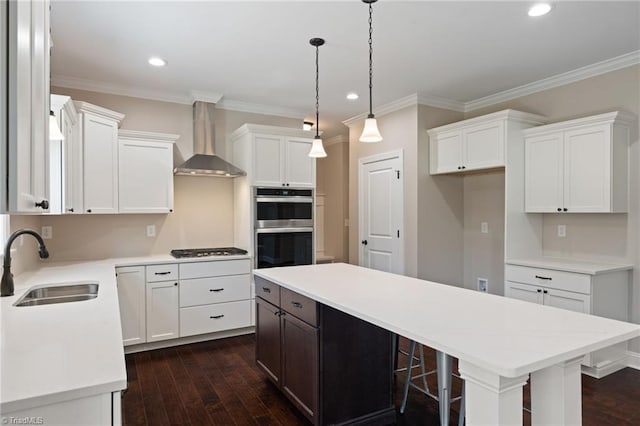 kitchen with stainless steel appliances, a center island, sink, white cabinets, and wall chimney range hood