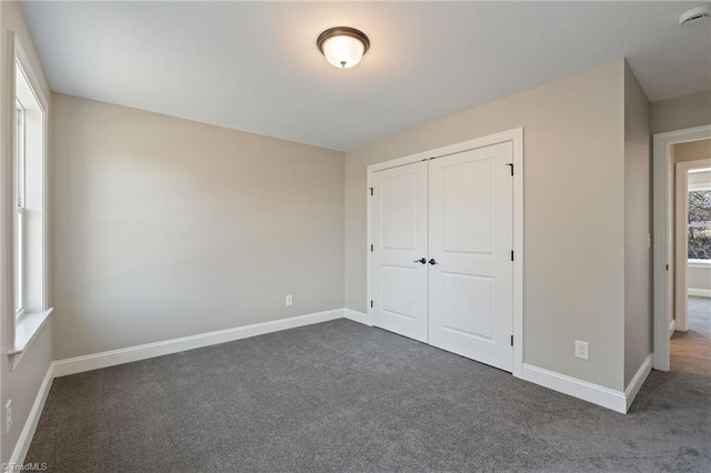 unfurnished bedroom with dark colored carpet and a closet