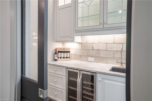 bar with light stone counters, beverage cooler, sink, and decorative backsplash