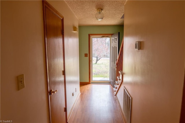 doorway featuring light wood-type flooring, visible vents, a textured ceiling, and baseboards