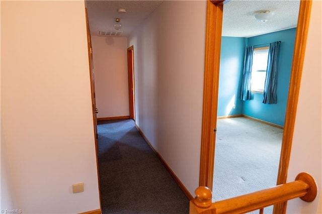 hallway with a textured ceiling, carpet, visible vents, and baseboards