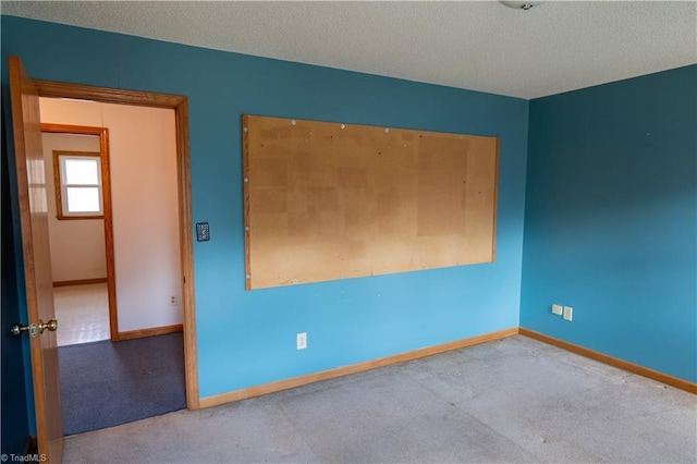 unfurnished room with a textured ceiling, carpet floors, and baseboards