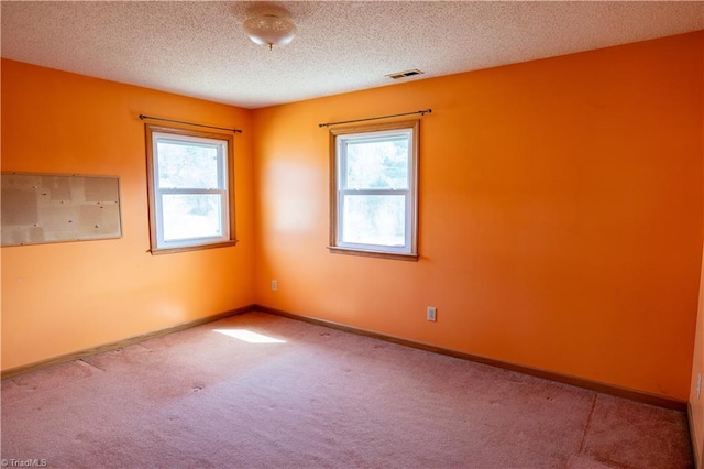 carpeted spare room featuring a healthy amount of sunlight, visible vents, baseboards, and a textured ceiling