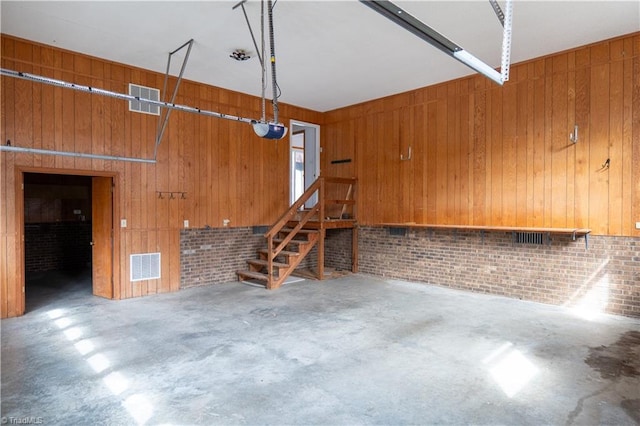 unfurnished living room with a garage, wood walls, and visible vents