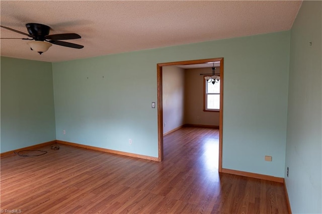 spare room with a textured ceiling, wood finished floors, a ceiling fan, and baseboards