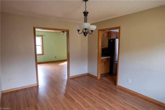 empty room featuring a textured ceiling, light wood-type flooring, and baseboards