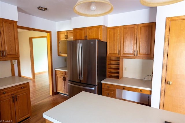 kitchen with brown cabinetry, light countertops, dark wood finished floors, and freestanding refrigerator